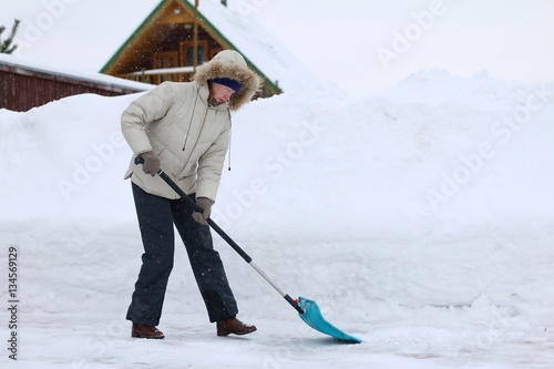 Женщина чистит лопатой дорожки от снега перед домом.