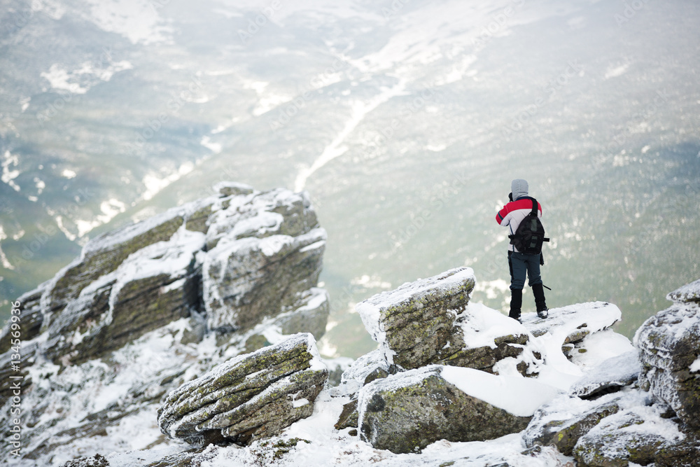 Hiker standing on a rock. Winter landscape. Shot of a young hiker taking photos from the top of a mountain Hiker standing on a rock. Winter landscape. Shot of a young hiker taking photos from the top of a mountain