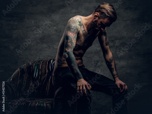 Tattooed bearded male sits on a chair. © Fxquadro