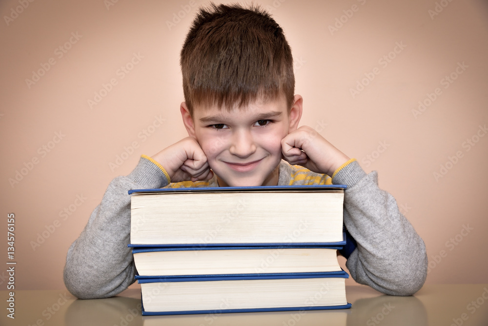 Smiling young boy sitting at the table and leaning his head on the books Smiling young boy sitting at the table and leaning his head on the books