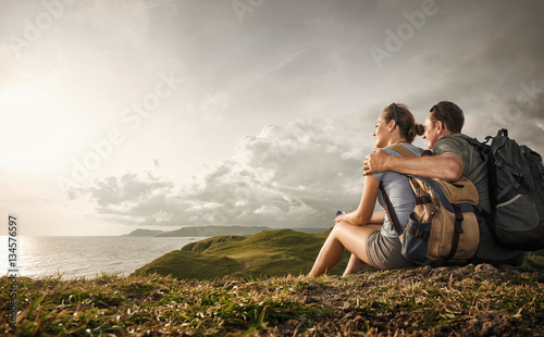 фотография Couple tourists with backpacks enjoying sunset on top of a mountain