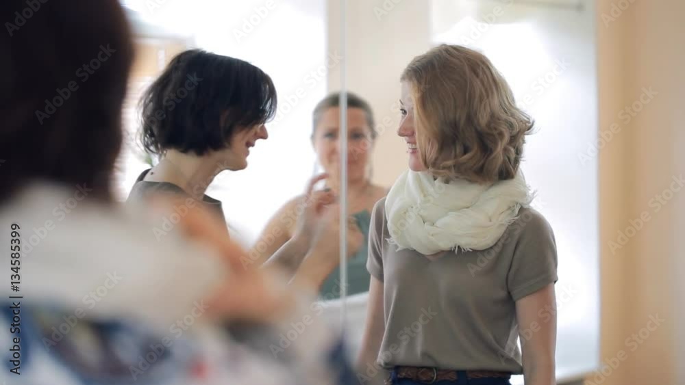 Image course lesson how to tie a scarf,neckerchief with a stylist. Professional image maker advise three women who look in a mirror to bend a shawl. She is wearing a wide light blue bracelet, a black Image course lesson how to tie a scarf,neckerchief with a stylist. Professional image maker advise three women who look in a mirror to bend a shawl. She is wearing a wide light blue bracelet, a black