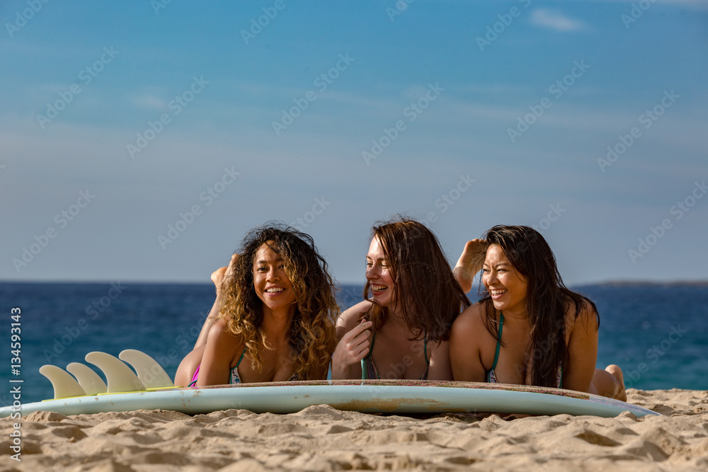 Three surfer girls lying on a surfing board having fun at a beach in sand.  Blue ocean background Stock Photo | Adobe Stock