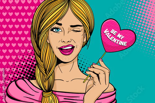 Pop art face. Young sexy blonde woman with pink paper with Be my Valentine lettering heart in her hand smiles and winks on dots background. Holiday party invitation vector poster in retro comic style.
