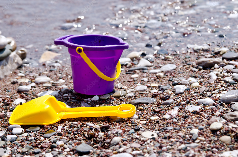 Small baby toy bucket and yellow shovel lying on the beach by the water. Small baby toy bucket and yellow shovel lying on the beach by the water.
