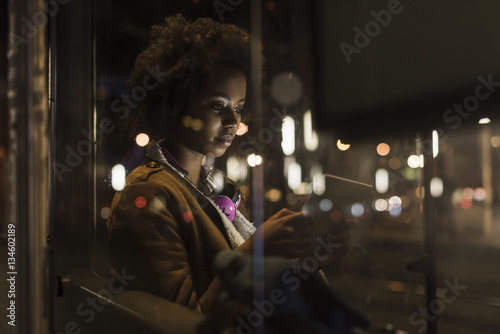 Young woman with tablet waiting at the tram stop by night photo