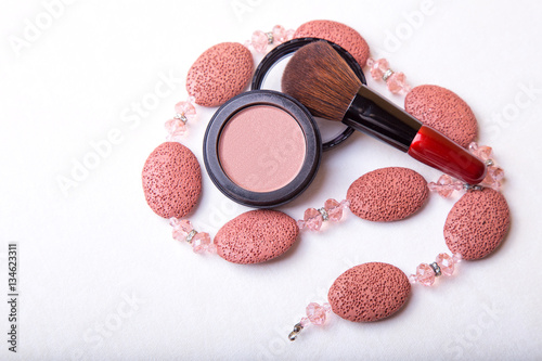 Overhead close up of one open jar of spilled pink blush powder with thick tipped brush on a white background