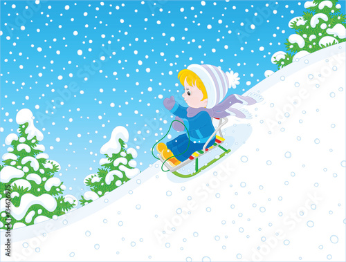 Small child sliding down the snowy hill on a sledge