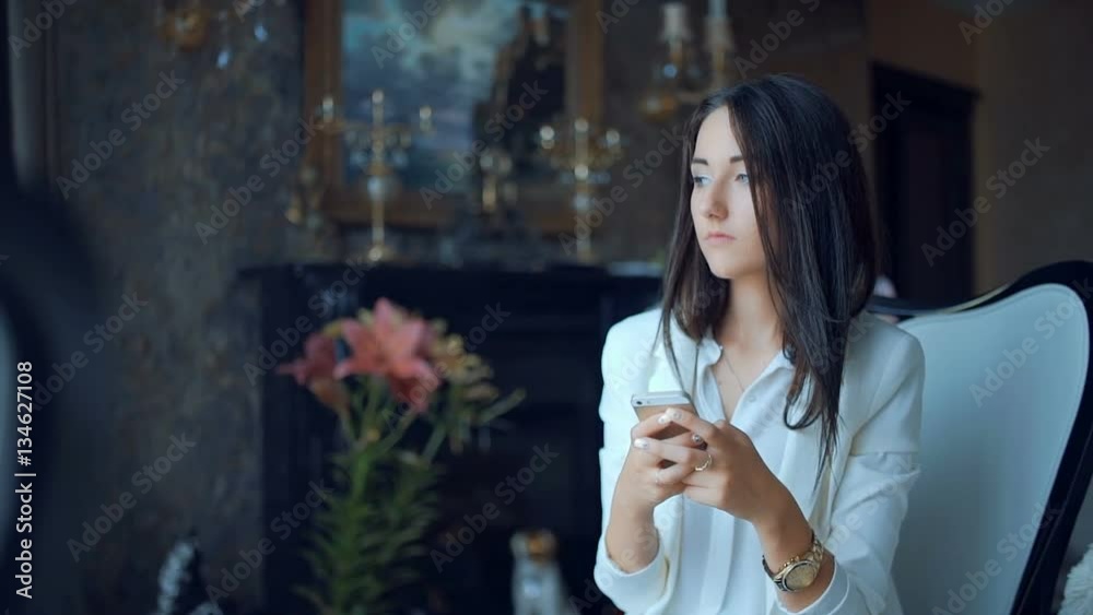 Woman texting with a smart phone sitting on a chair in the living room in a house interior Woman texting with a smart phone sitting on a chair in the living room in a house interior