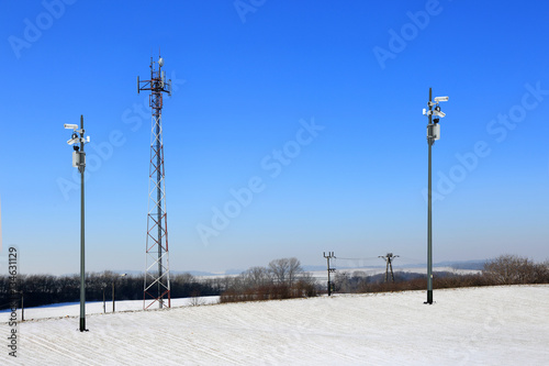 Antena, kamery i maszty z antenami satelitarnymi przy ośnieżonym polu.