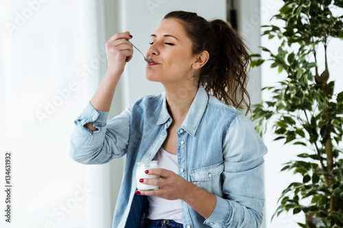Beautiful young woman eating yogurt at home. photo
