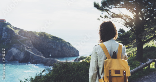 Hipster young girl with backpack enjoying sunset on seascape on mountain. Tourist traveler on background landscape view mockup. Hiker looking ocean in trip holiday in basque island