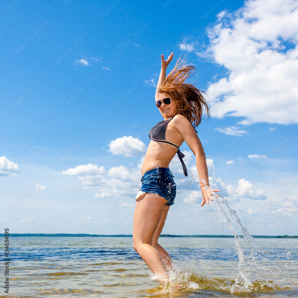 Naklejka premium Beautiful young sexy model in the sea. Lovely young woman jumping on the sunny beach