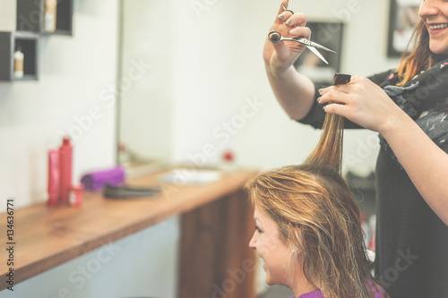 Cheerful hairdresser cutting woman hair for a new haircut style