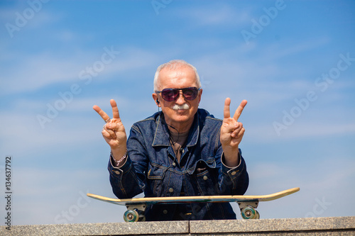 happy old man showing thumbs up. The concept of life satisfaction. Portrait of a positive gray-haired man with a skateboard. winner concept.