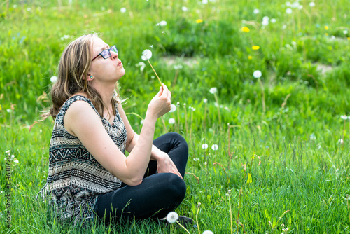 Beautiful woman blowing dandelion on meadow in spring