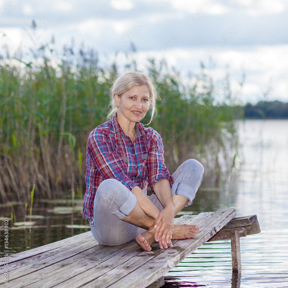 Fototapeta premium middle-aged woman on the pier. Concept joyful elderly. Portrait of happy middle aged woman sitting on the beach.