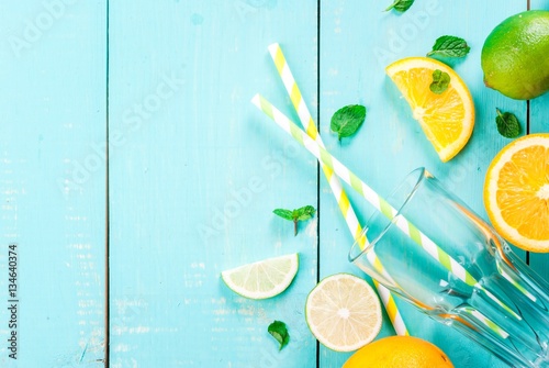 Ingredients for citrus juice or a refreshing summer cocktail: orange, lime, mint leaves, along with a glass and drinking straws, top view, copy space