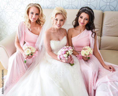 Beautiful bride and bridesmaids in pink dresses sit on soft couc photo