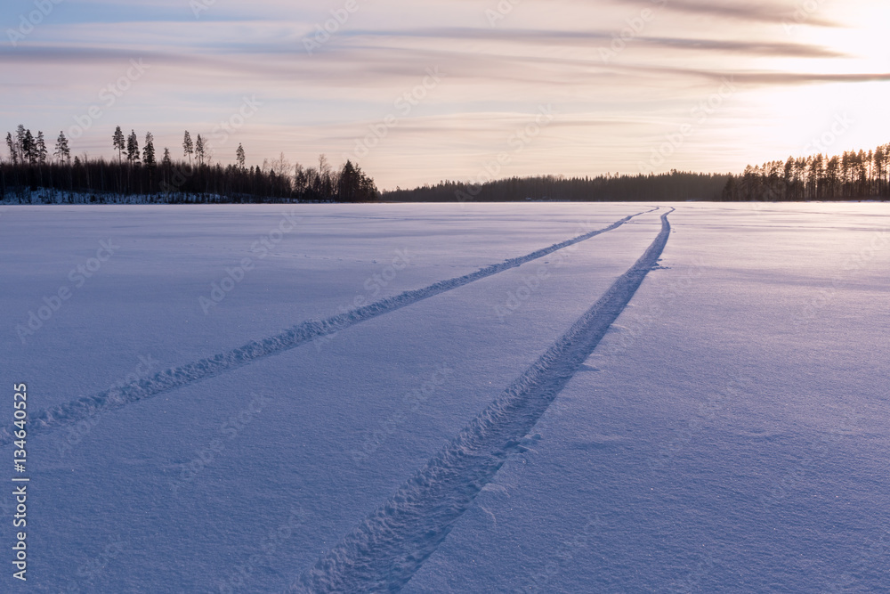Car tire tracks on snow cover at a lake