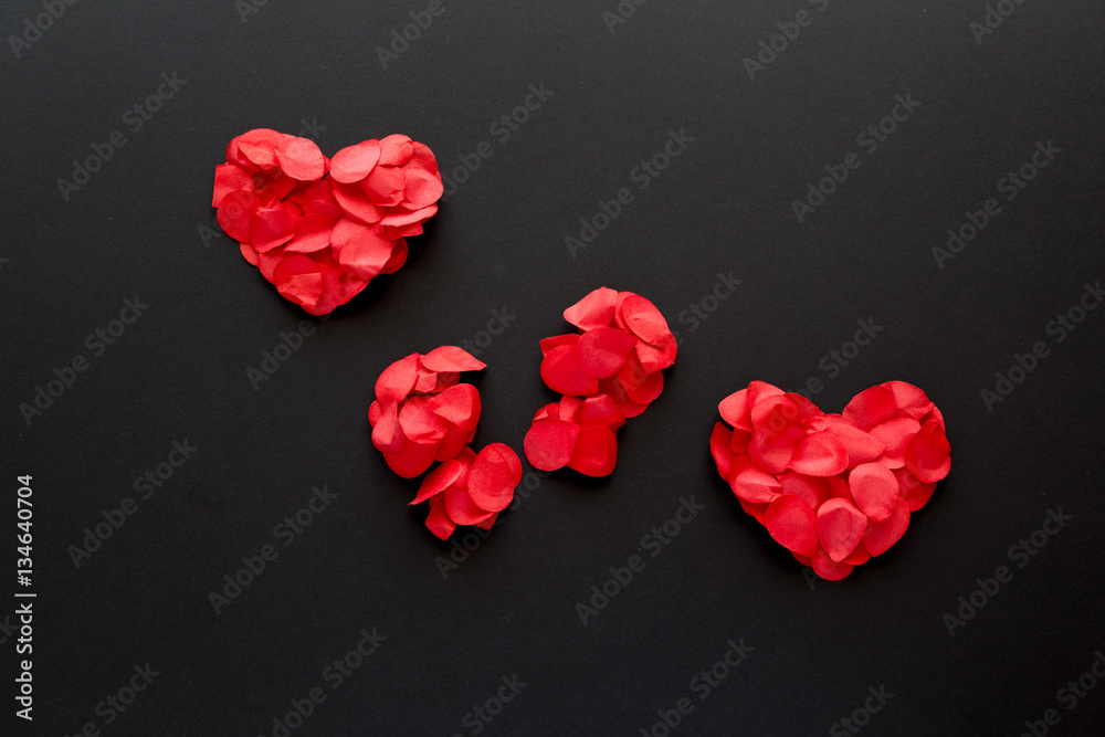 Due cuori di petali rossi con al centro un cuore spezzato su sfondo nero  Stock Photo