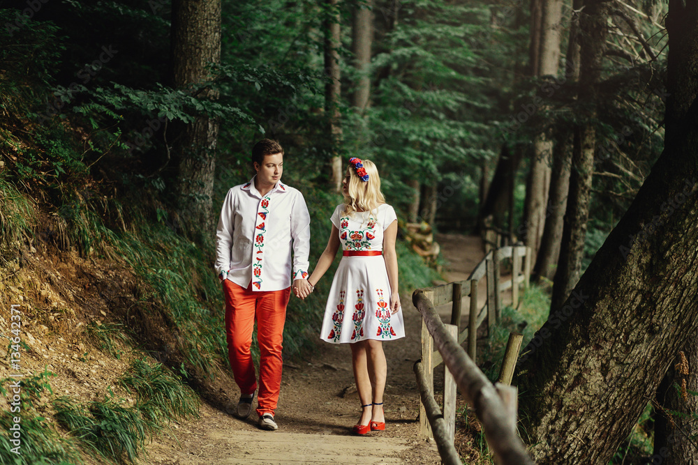 Fototapeta premium Man and woman in embroidered clothes walk along wooden path in t