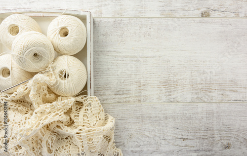 crochet tablecloth, crochet hooks and balls of cotton thread on a white wooden table  flat lay. Top view, copy space.