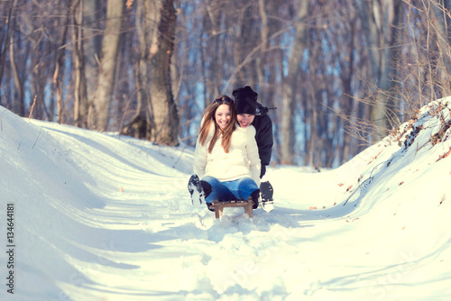 Young playful couple having fun sledging down snow covered hill