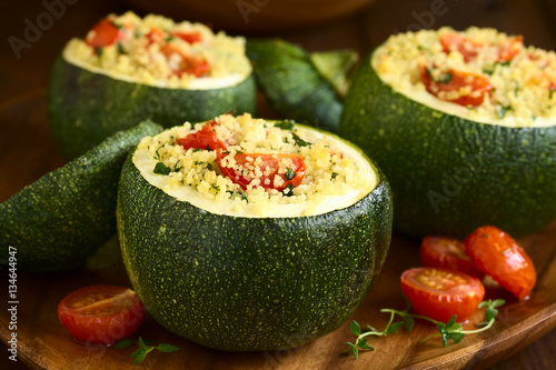Baked round zucchini stuffed with couscous, cherry tomato and parsley, photographed with natural light (Selective Focus on the cherry tomato on the first stuffed zucchini)