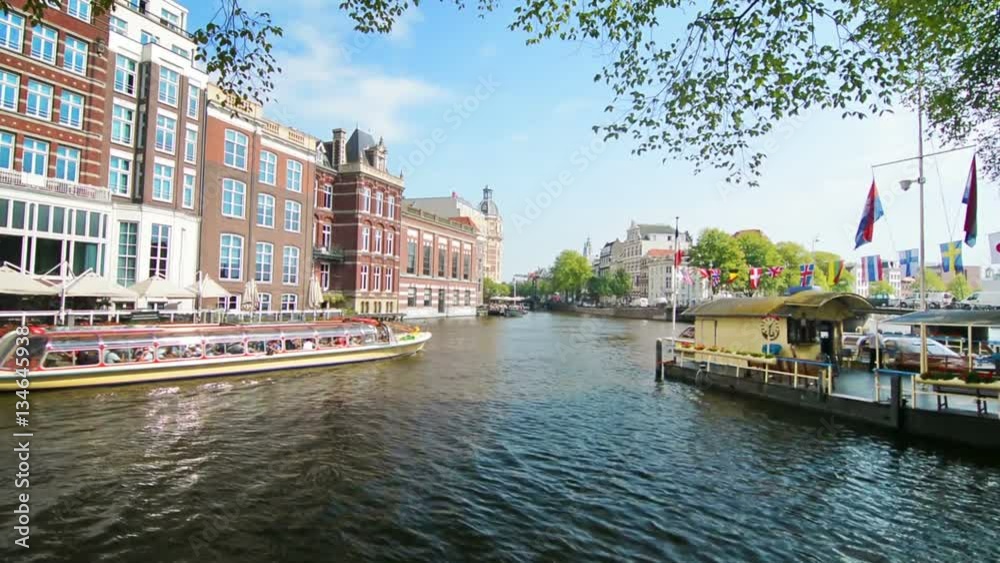 Tour boat sails in Amsterdam canal on a sunny day. Tour boat sails in Amsterdam canal on a sunny day.