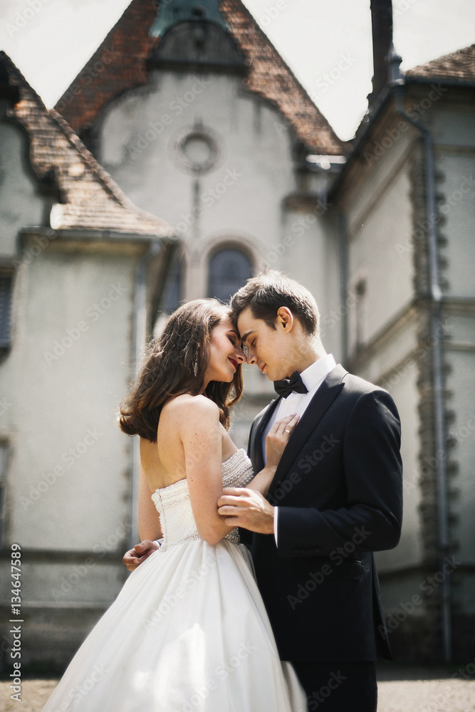 Handsome groom holds bride tender in his arms standing before ol Handsome groom holds bride tender in his arms standing before ol