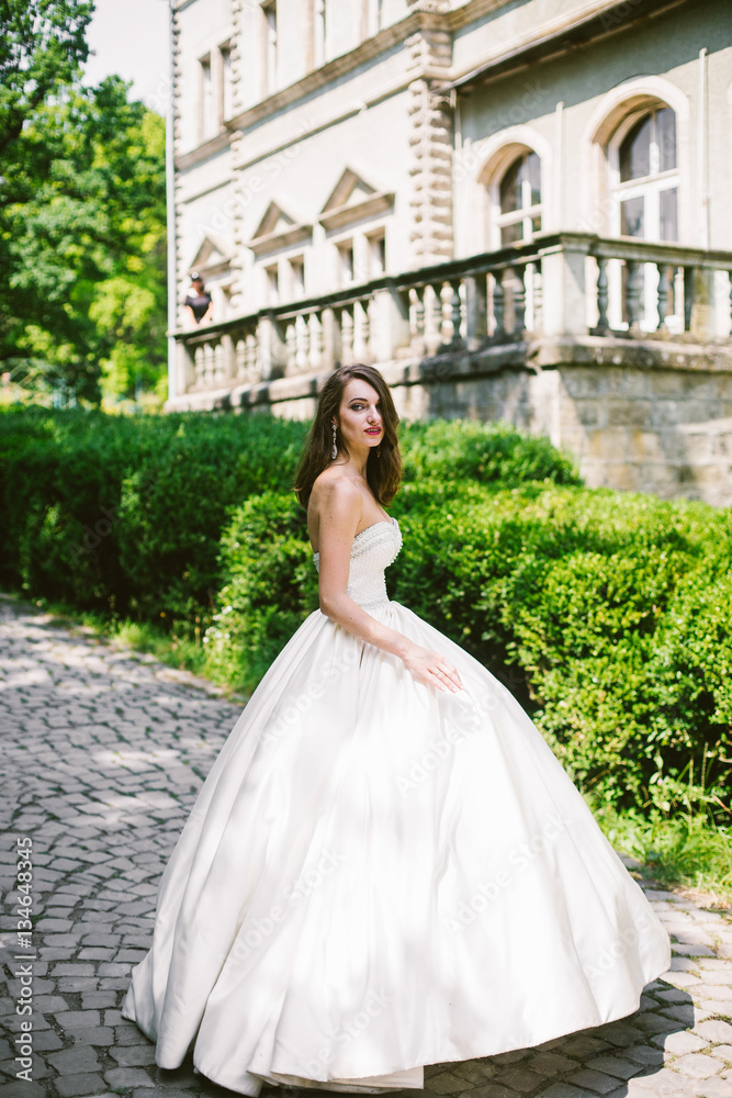 Elegant bride in luxurious ivory dress stands on path along gree