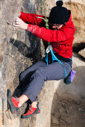 Young caucasian woman dressed for cold weather climbs a granite cliff in the desert late in the afternoon