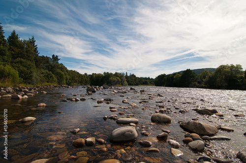 Salmon river in Scotland with pebbled banks and blue sky to background photo