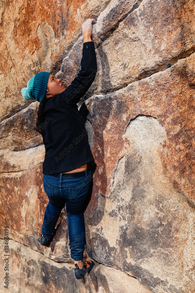 Young african american woman climbs along a granite cliff in the desert dressed for cold weather
