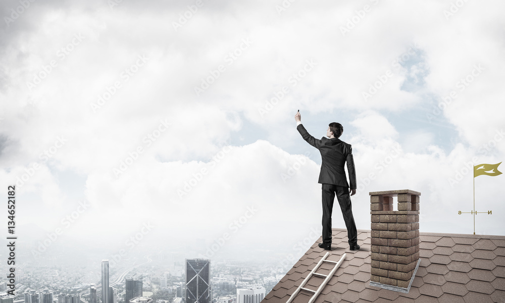 Businessman on house roof touch empty space. Mixed media Businessman on house roof touch empty space. Mixed media