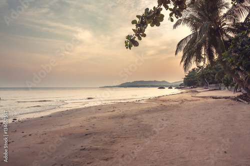 Deserted tropical beach landscape during sunset with beautiful scenic view on sea and coastline with palm trees and sunset sky