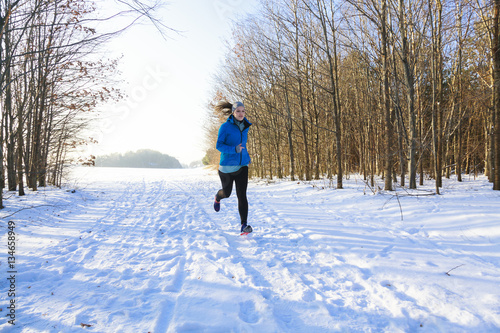 Jogging femal from left to right in winter with forest in background and sun from left 