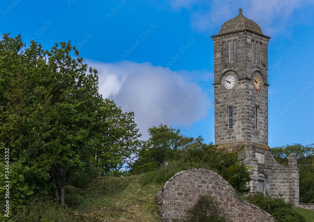 Helmsdale, Scotland - June 4, 2012: The Great War Memorial and gray stone Clock Tower stands on a hill just outside the town. Green vegetation and blue sky.