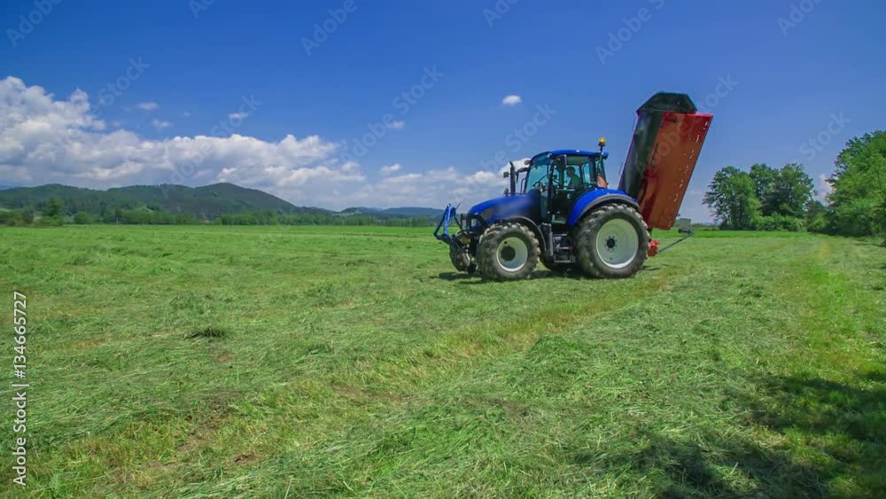 A big blue tractor is slowly arriving on a grass field. There is also agricultural machinery connected to it.
A big blue tractor is slowly arriving on a grass field. There is also agricultural machinery connected to it.