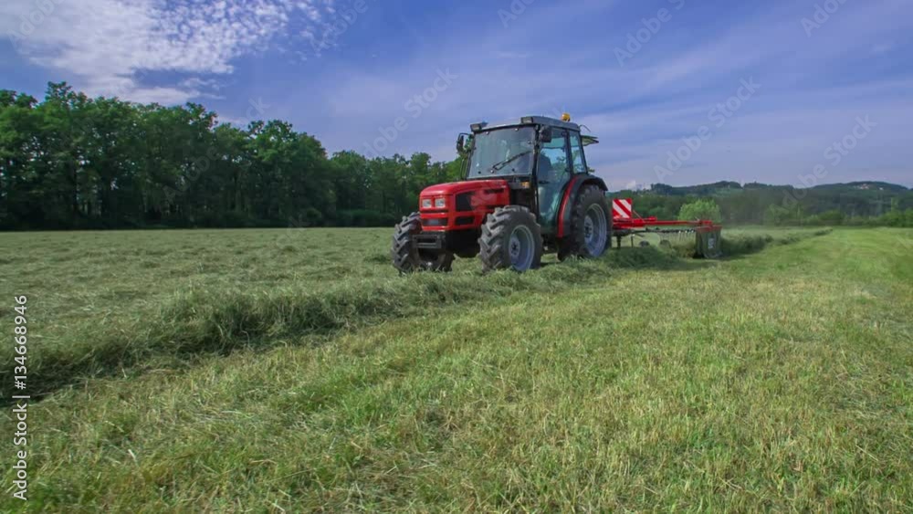 A farmer sitting in his tractor is driving across the field and he is preparing hay. The day is sunny and wonderful.
A farmer sitting in his tractor is driving across the field and he is preparing hay. The day is sunny and wonderful.