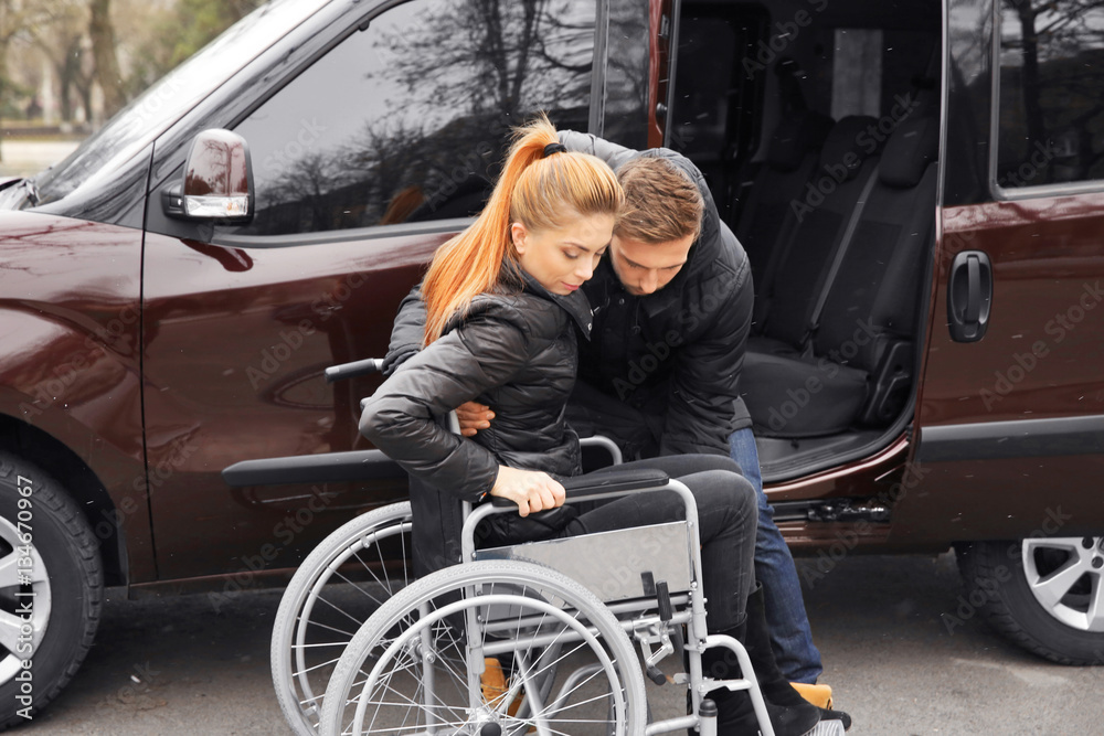 Young man helping handicapped woman to sit in wheelchair Young man helping handicapped woman to sit in wheelchair
