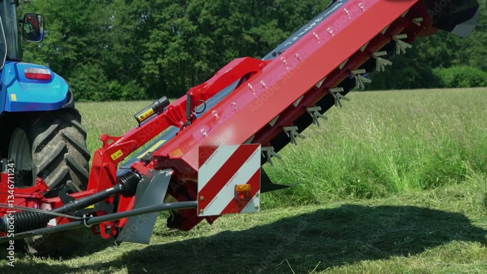 A farmer is sitting on his blue tractor, he pushes a button and he starts lowering down a grass cutting machine. In the background, grass is swaying in the wind.
A farmer is sitting on his blue tractor, he pushes a button and he starts lowering down a grass cutting machine. In the background, grass is swaying in the wind.