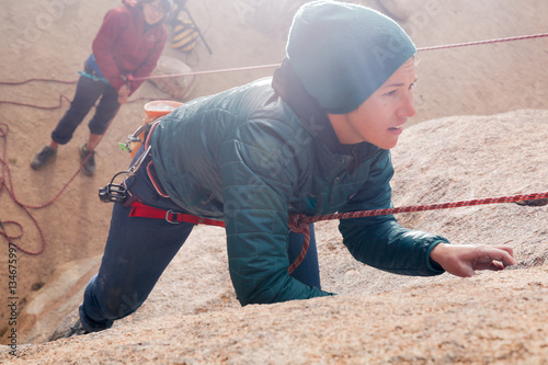 Young caucasian woman dressed for cold weather rock climbing in the desert climbs a cliff