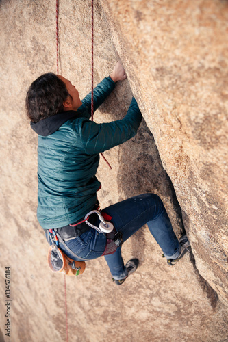 Young caucasian woman dressed for cold weather rock climbing in the desert climbs a cliff