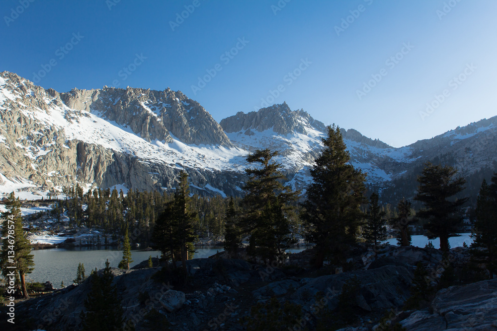 Snow covered granite peaks and cliffs during Spring in California's Sierra Nevada mountains surrounding an alpine lake