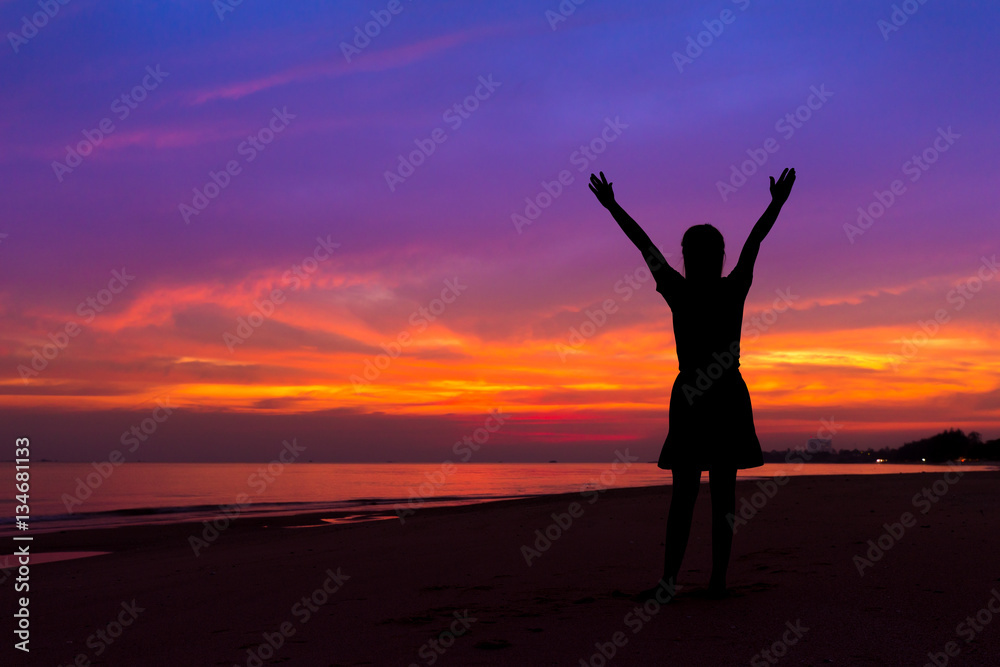Silhouette of woman with hands up while standing on sea beach at Silhouette of woman with hands up while standing on sea beach at