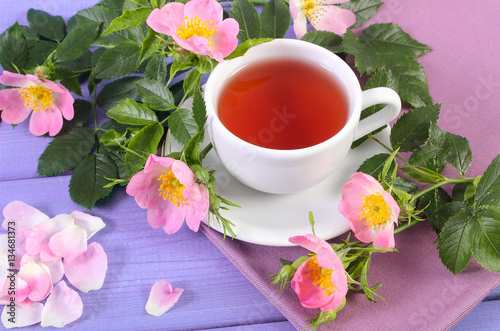 Cup of tea and wild rose flower on purple boards