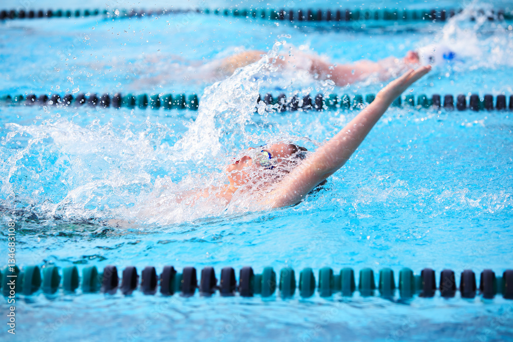 Motion blur image of a boy swimming backstroke in a race.