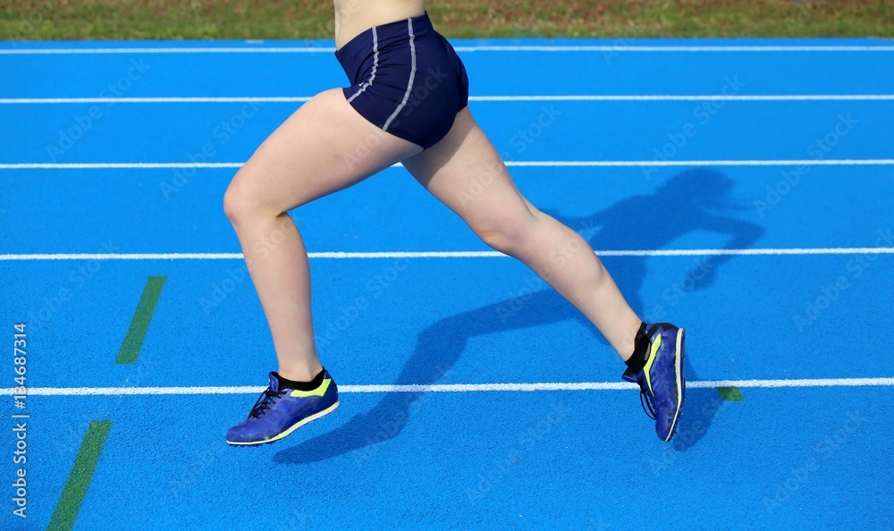 Fototapeta legs of young female runner running on athletic track